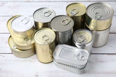 Photo of Many closed tin cans on white wooden table, closeup