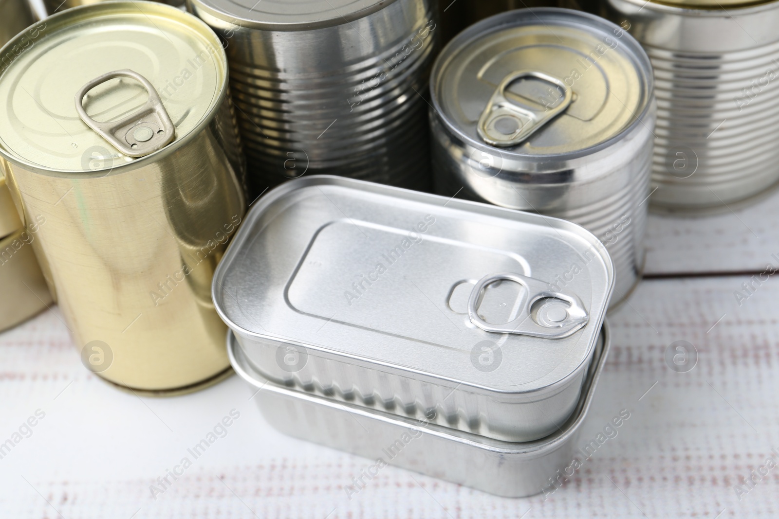 Photo of Many closed tin cans on white wooden table, closeup