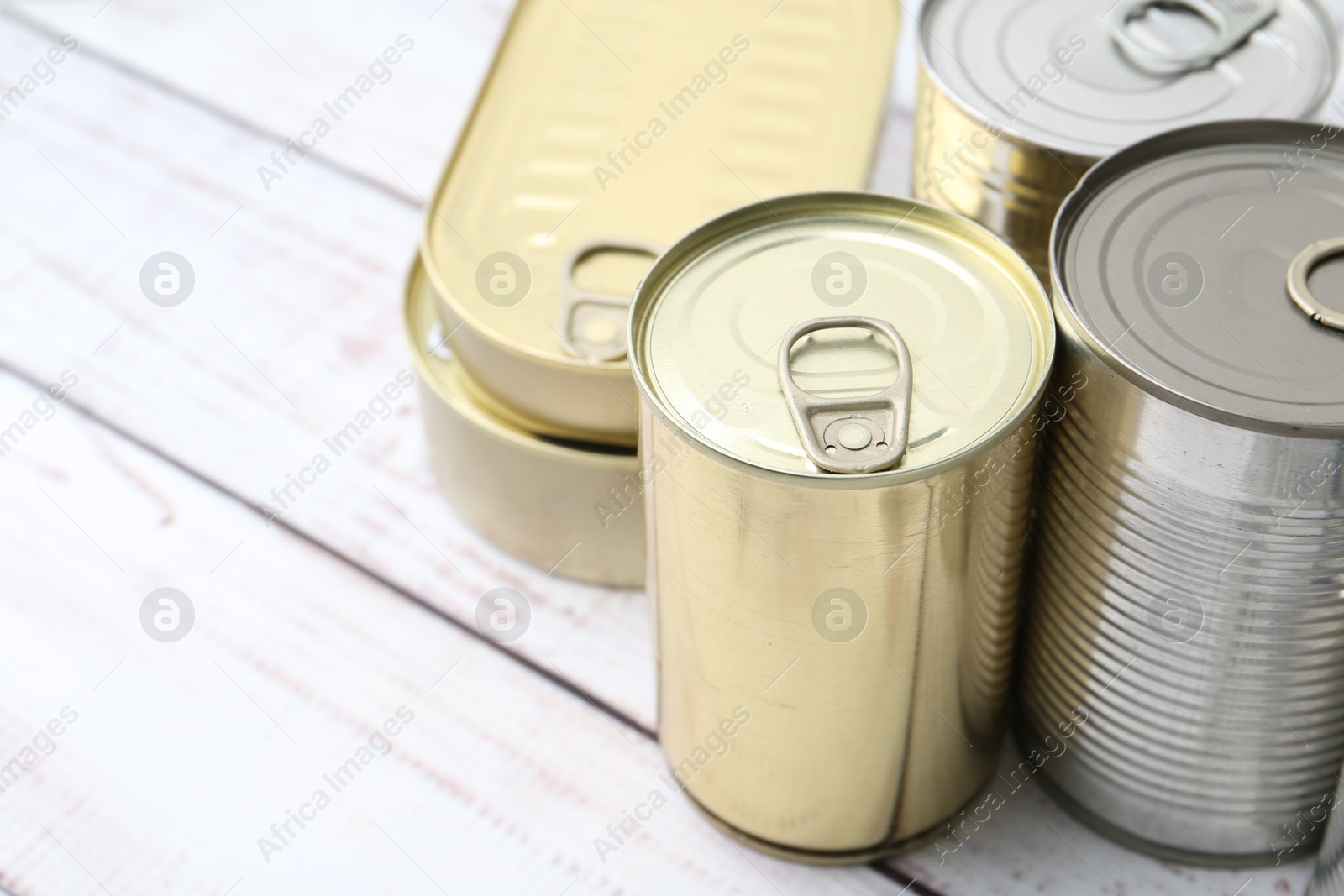 Photo of Many closed tin cans on white wooden table, closeup. Space for text