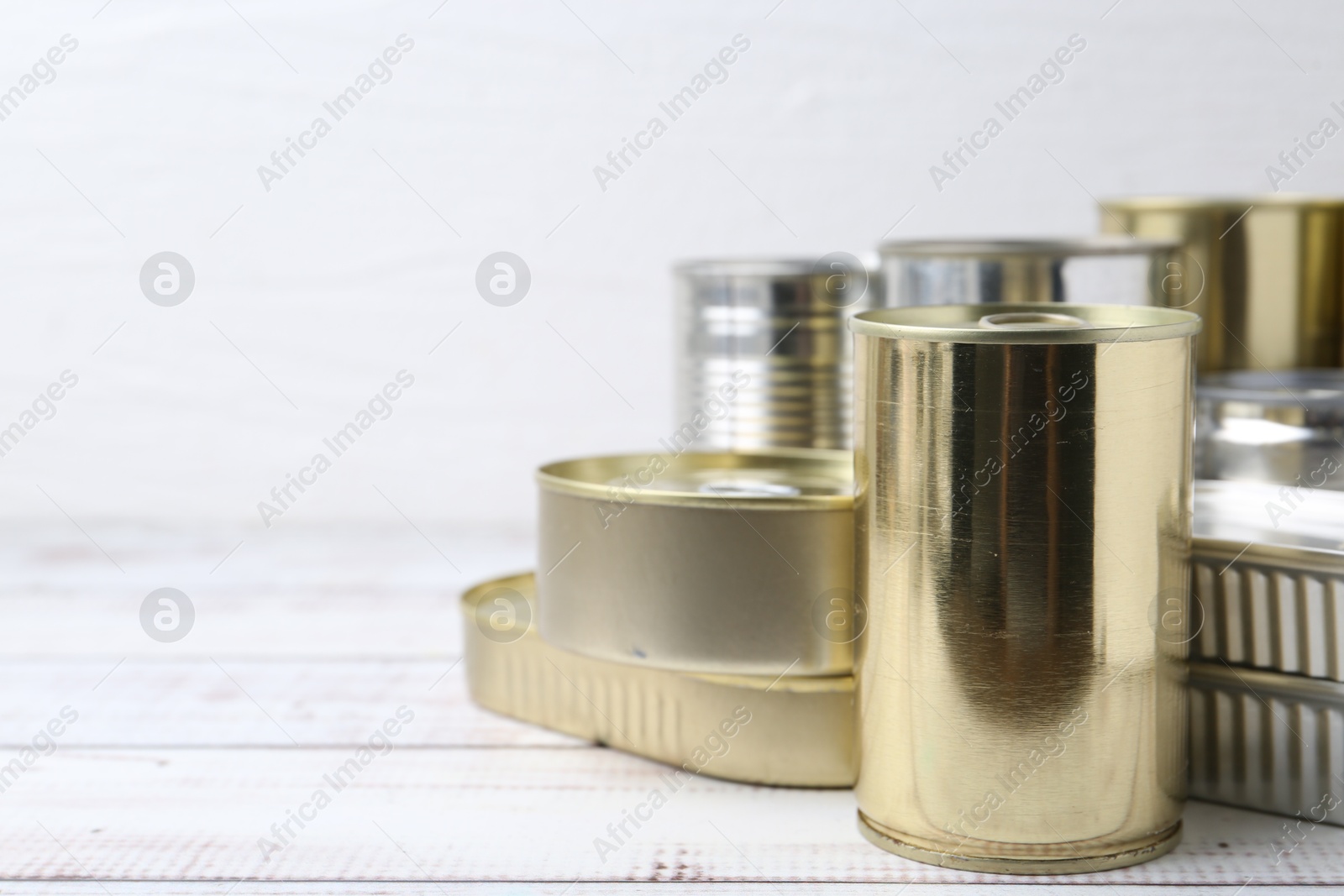 Photo of Many closed tin cans on white wooden table, closeup. Space for text