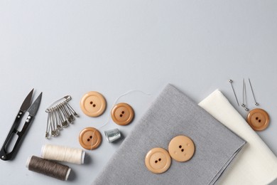 Photo of Different sewing supplies and fabric on light grey background, flat lay. Space for text