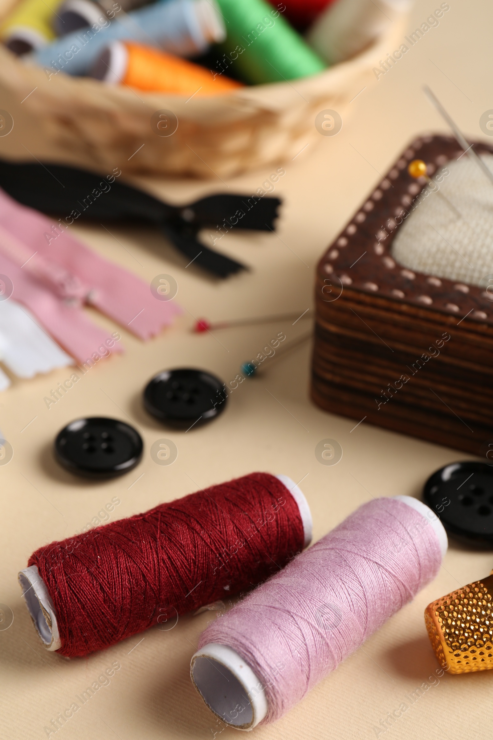 Photo of Different sewing supplies on beige background, closeup