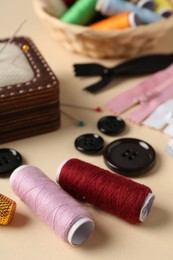 Photo of Different sewing supplies on beige background, closeup