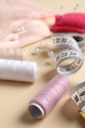 Photo of Different sewing supplies on beige background, closeup