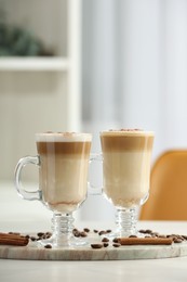 Photo of Tasty latte macchiato, coffee beans and cinnamon sticks on white table, space for text