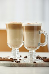 Photo of Tasty latte macchiato, coffee beans and cinnamon sticks on white table, closeup