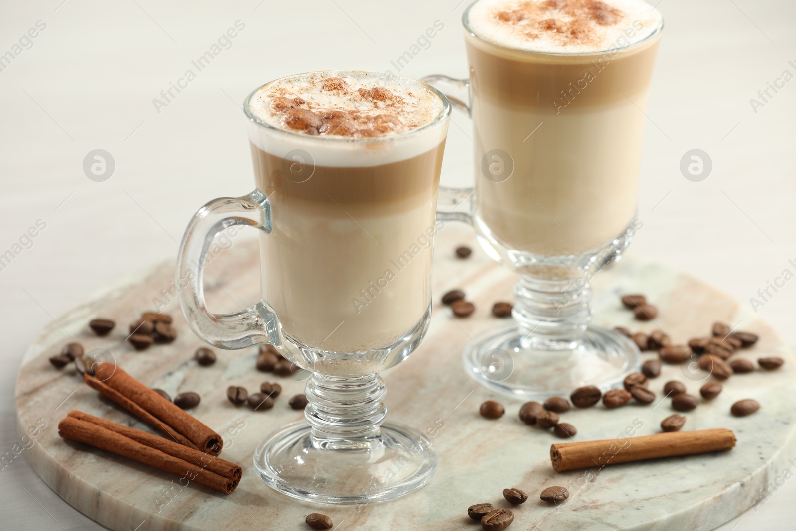 Photo of Tasty latte macchiato, coffee beans and cinnamon sticks on white table, closeup