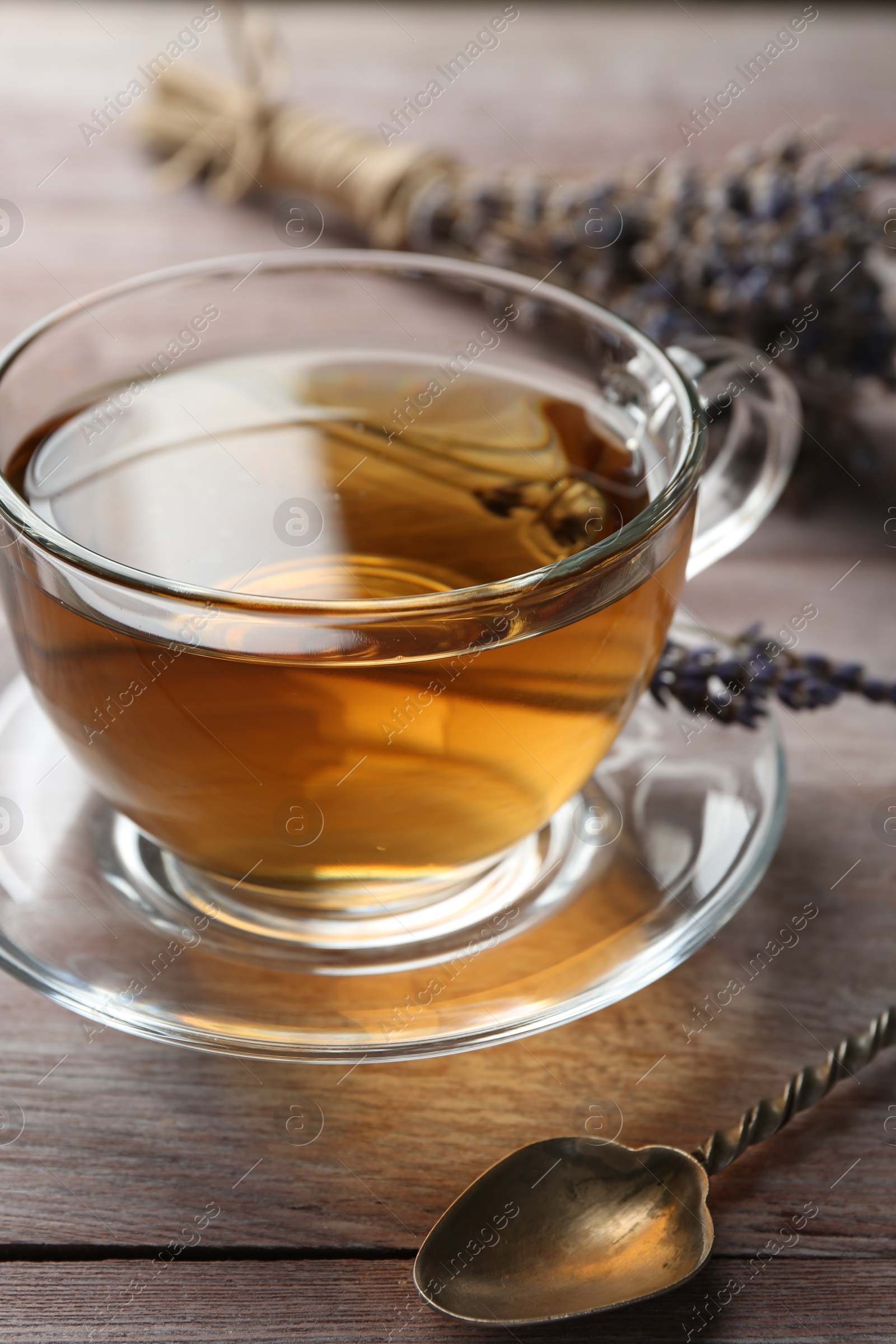 Photo of Aromatic lavender tea in glass cup, spoon and dry flowers on wooden table, closeup