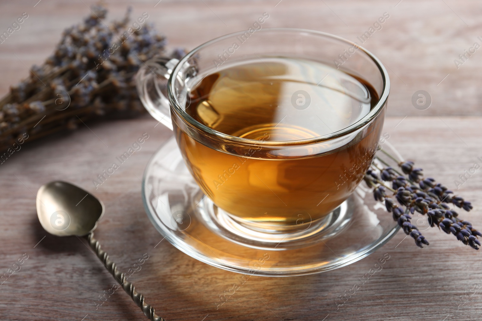 Photo of Aromatic lavender tea in glass cup, spoon and dry flowers on wooden table, closeup