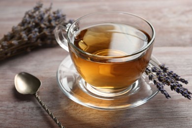 Aromatic lavender tea in glass cup, spoon and dry flowers on wooden table, closeup