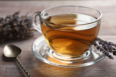 Photo of Aromatic lavender tea in glass cup, spoon and dry flowers on wooden table, closeup