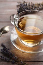 Aromatic lavender tea in glass cup and dry flowers on wooden table, closeup