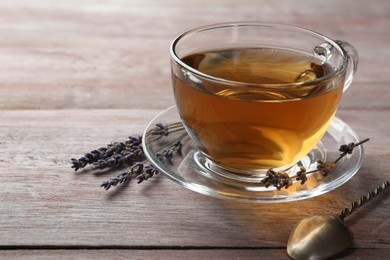 Photo of Aromatic lavender tea in glass cup and dry flowers on wooden table, closeup. Space for text