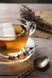 Photo of Aromatic lavender tea in glass cup, spoon and dry flowers on wooden table, closeup