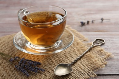 Aromatic lavender tea in glass cup, spoon and dry flowers on wooden table, closeup