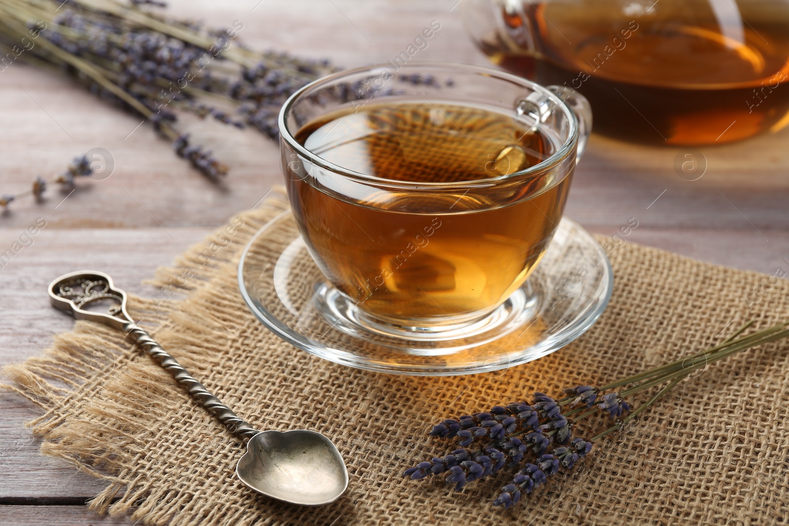 Photo of Aromatic lavender tea in glass cup, spoon and dry flowers on wooden table, closeup