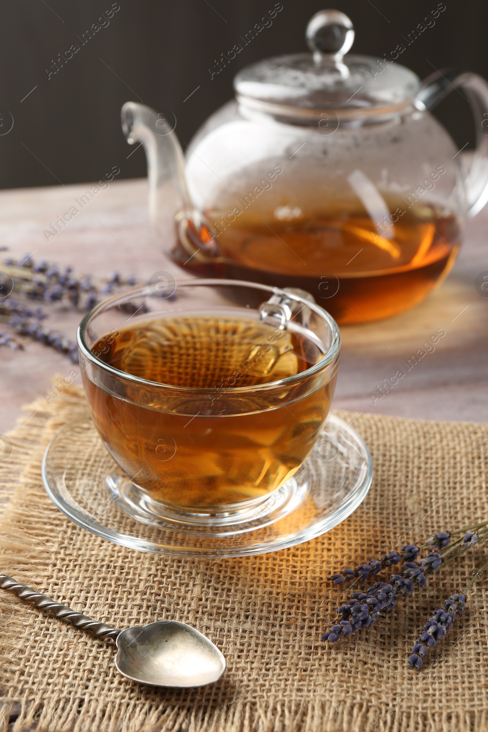 Photo of Aromatic lavender tea in glass cup, spoon and dry flowers on wooden table, closeup