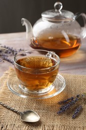 Photo of Aromatic lavender tea in glass cup, spoon and dry flowers on wooden table, closeup