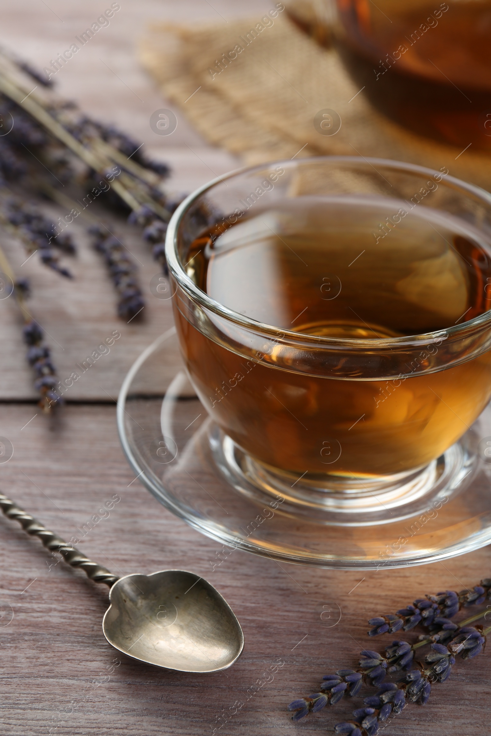 Photo of Aromatic lavender tea in glass cup, spoon and dry flowers on wooden table, closeup