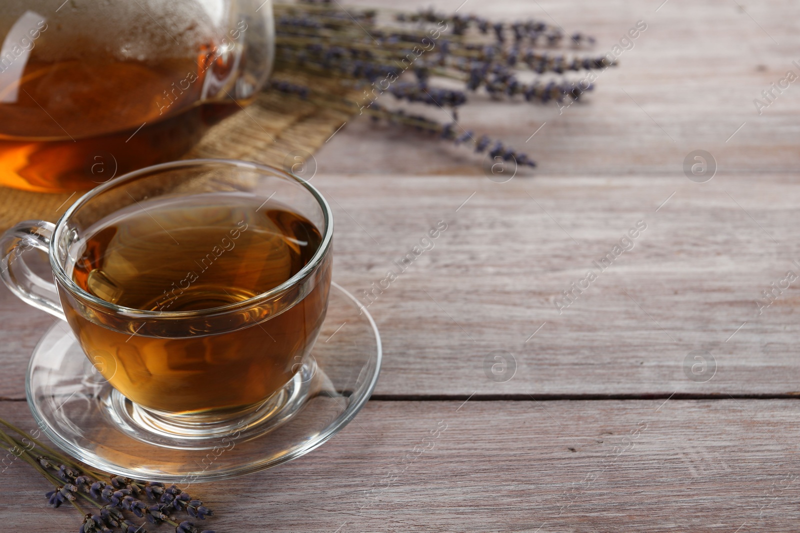 Photo of Aromatic lavender tea in glass cup and dry flowers on wooden table, closeup. Space for text