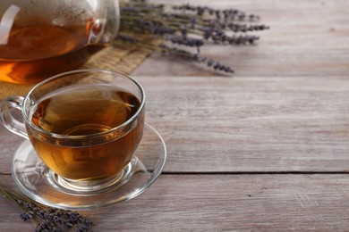 Photo of Aromatic lavender tea in glass cup and dry flowers on wooden table, closeup. Space for text