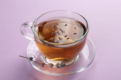 Aromatic lavender tea in glass cup and dry flower on pink background, closeup