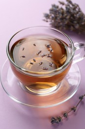 Aromatic lavender tea in glass cup and dry flowers on pink background, closeup