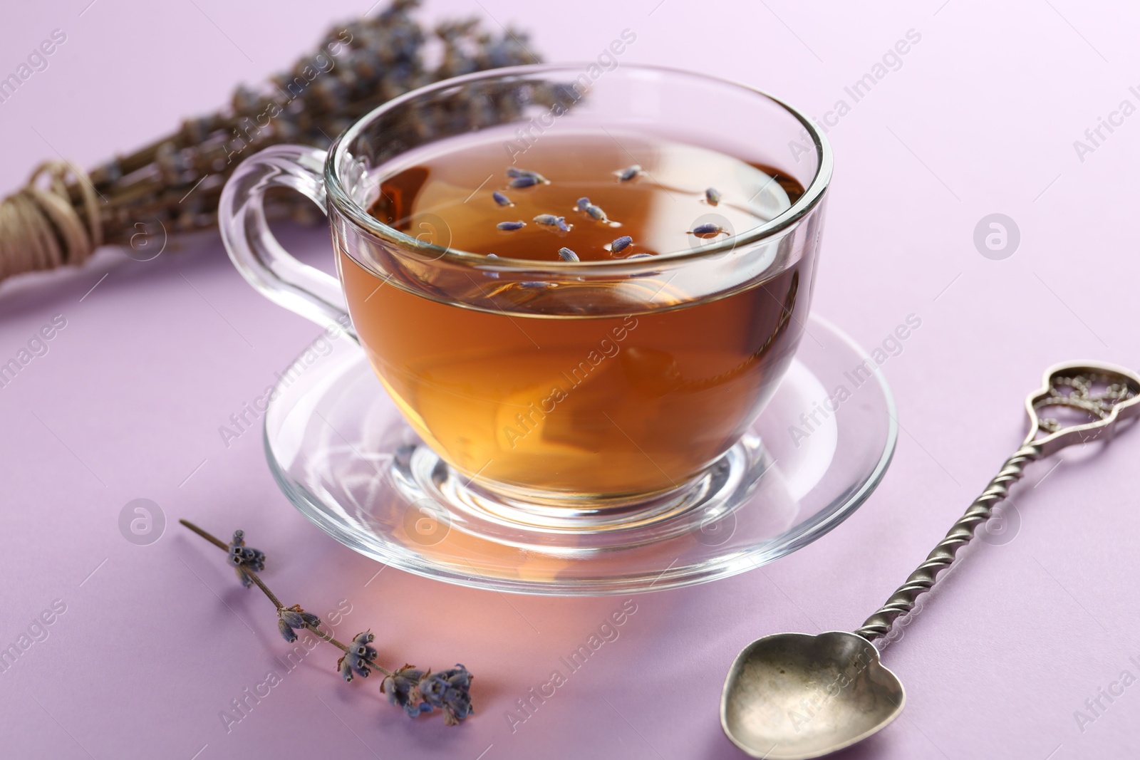 Photo of Aromatic lavender tea in glass cup, spoon and dry flowers on pink background, closeup