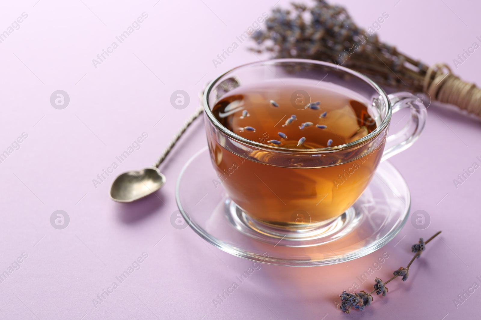 Photo of Aromatic lavender tea in glass cup, spoon and dry flowers on pink background, closeup. Space for text