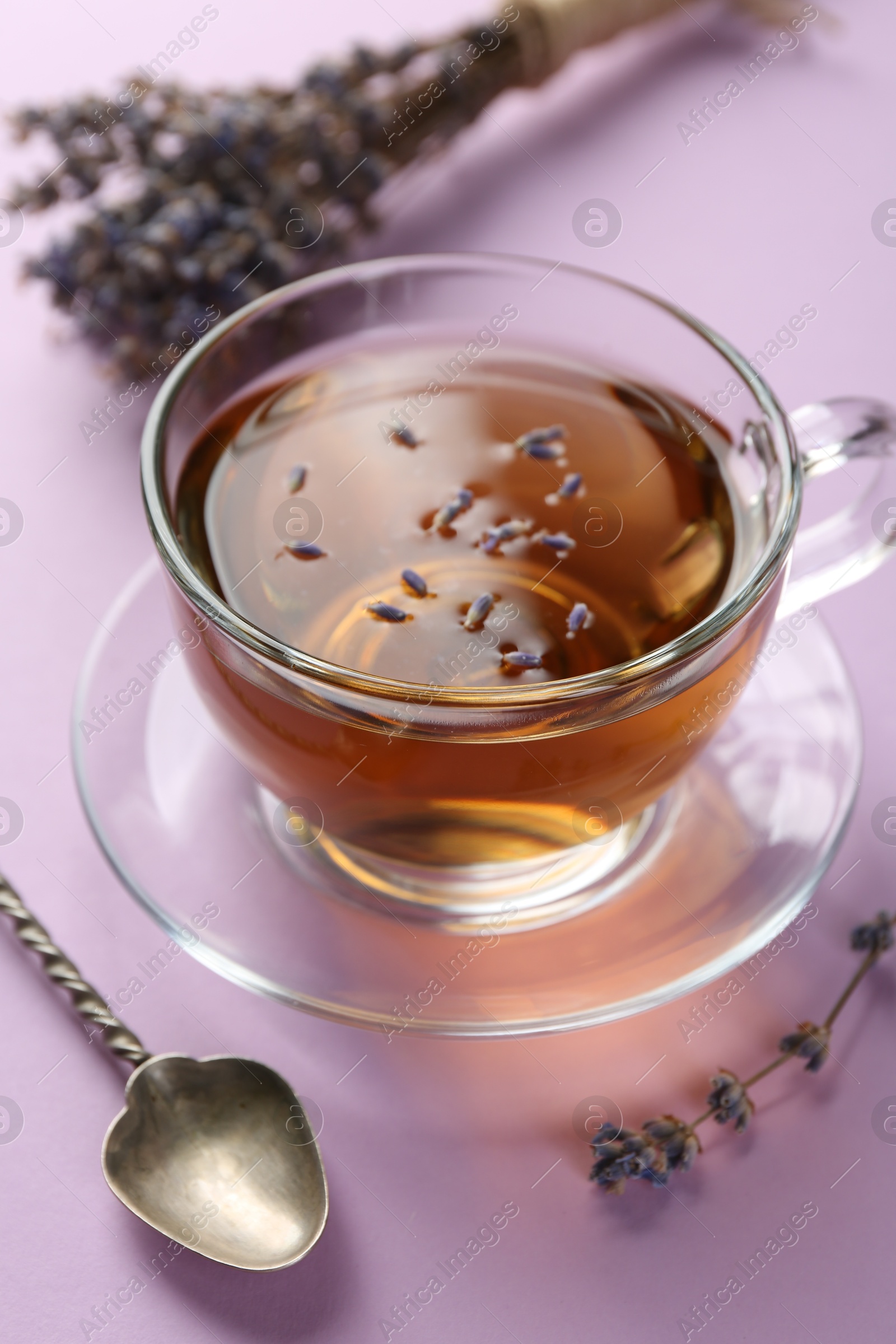 Photo of Aromatic lavender tea in glass cup, spoon and dry flowers on pink background, closeup