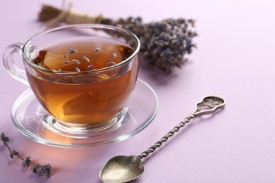 Aromatic lavender tea in glass cup, spoon and dry flowers on pink background, closeup. Space for text