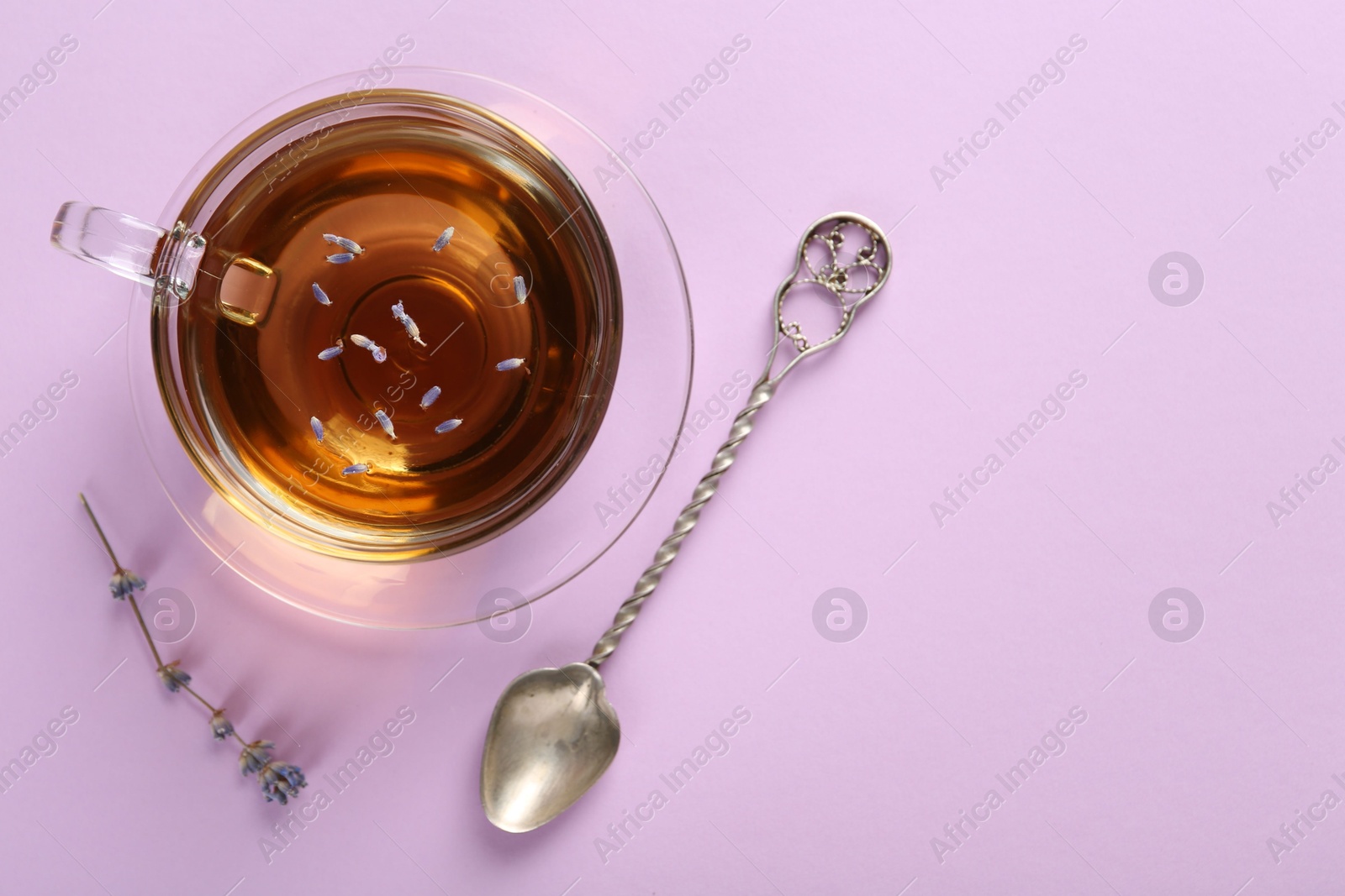 Photo of Aromatic lavender tea in glass cup, spoon and dry flower on pink background, top view. Space for text