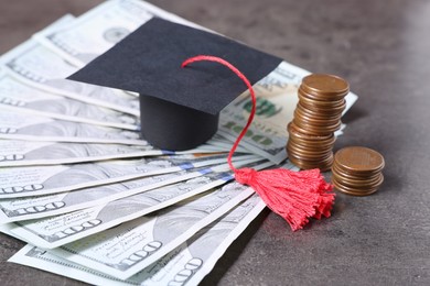 Photo of Graduate hat, dollars and coins on grey textured table. Tuition payment