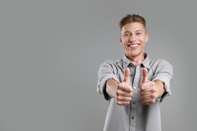 Photo of Happy man showing thumbs up on grey background, space for text. Like gesture