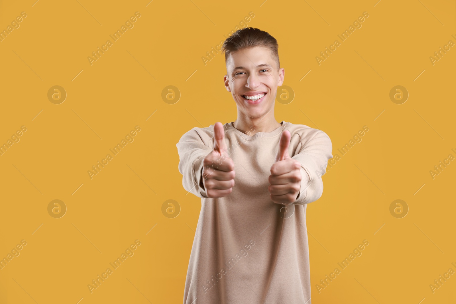 Photo of Happy man showing thumbs up on orange background, space for text. Like gesture