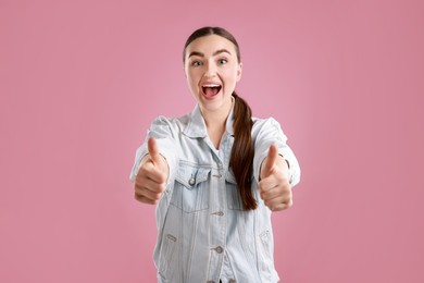 Photo of Emotional woman showing thumbs up on pink background. Like gesture