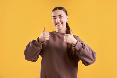 Photo of Happy woman showing thumbs up on yellow background. Like gesture