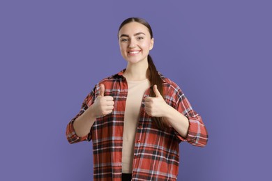 Photo of Happy woman showing thumbs up on purple background. Like gesture