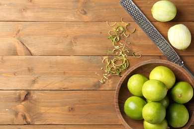 Photo of Lime zest, grater and fresh fruits on wooden table, flat lay. Space for text