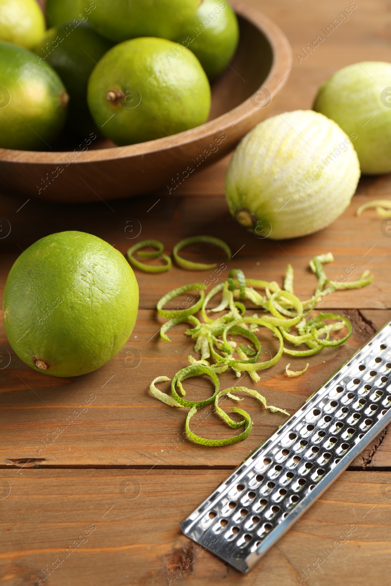 Photo of Lime zest, grater and fresh fruits on wooden table, closeup