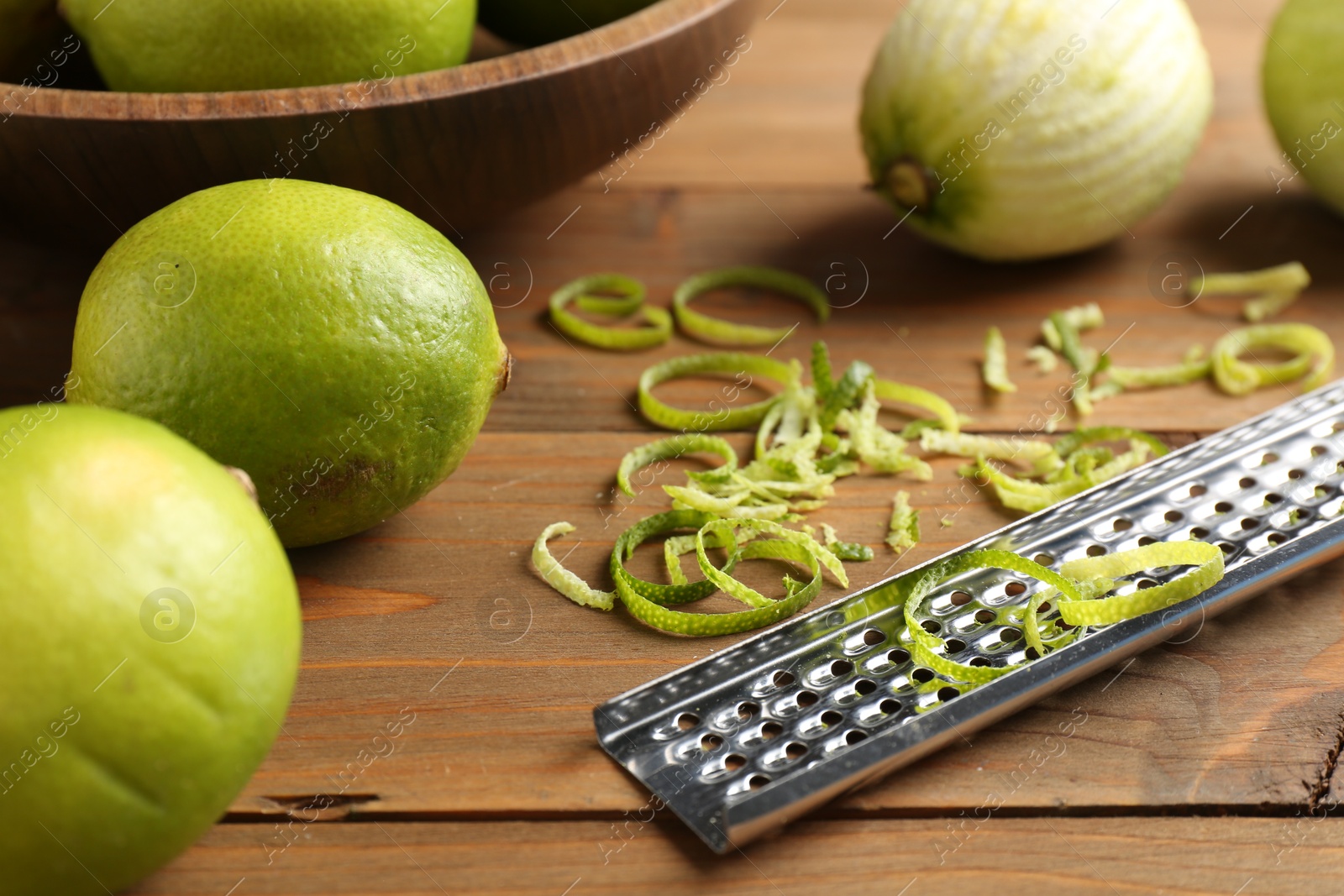 Photo of Lime zest, grater and fresh fruits on wooden table, closeup