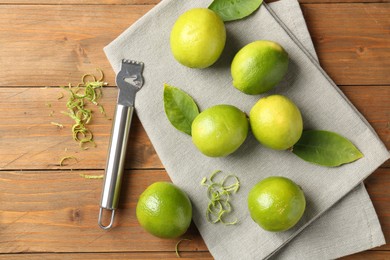 Photo of Lime zest, zester, leaves and fresh fruits on wooden table, flat lay