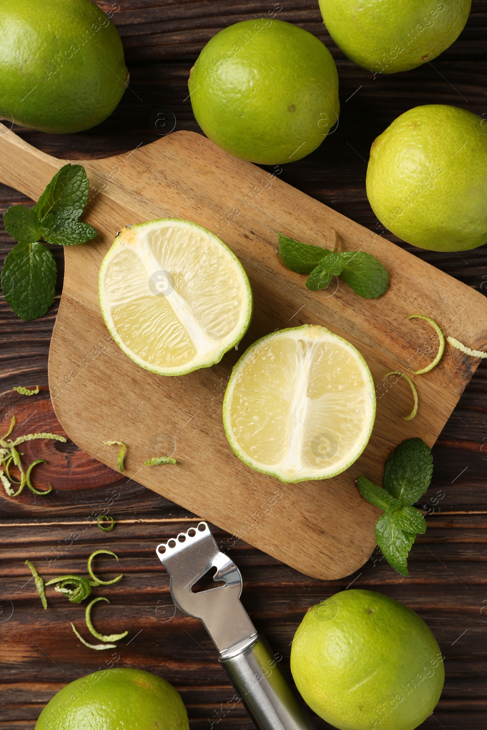 Photo of Lime zest, zester, mint leaves and fresh fruits on wooden table, flat lay