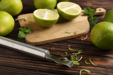 Photo of Lime zest, zester, mint leaves and fresh fruits on wooden table, closeup