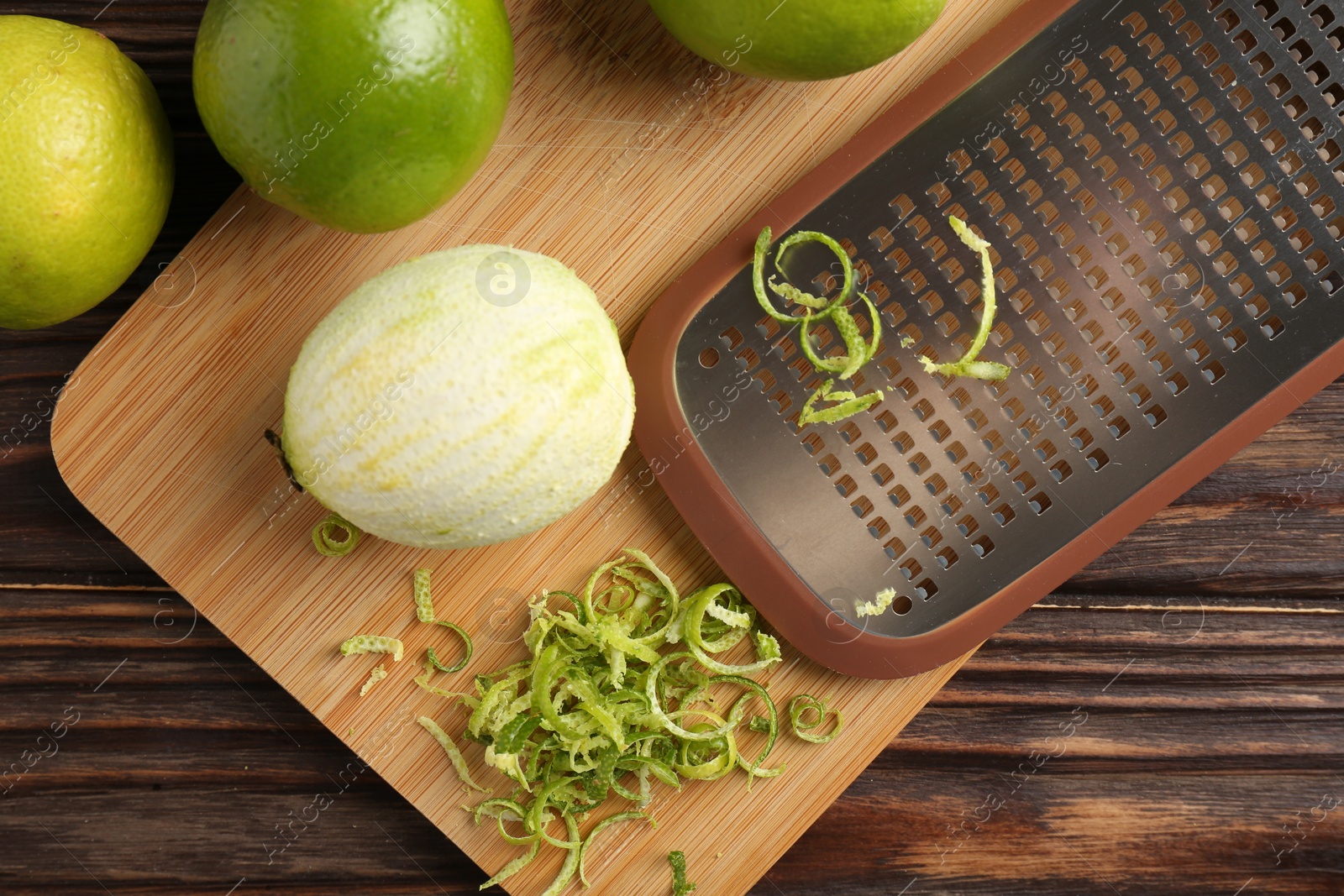 Photo of Lime zest, grater and fresh fruits on wooden table, flat lay