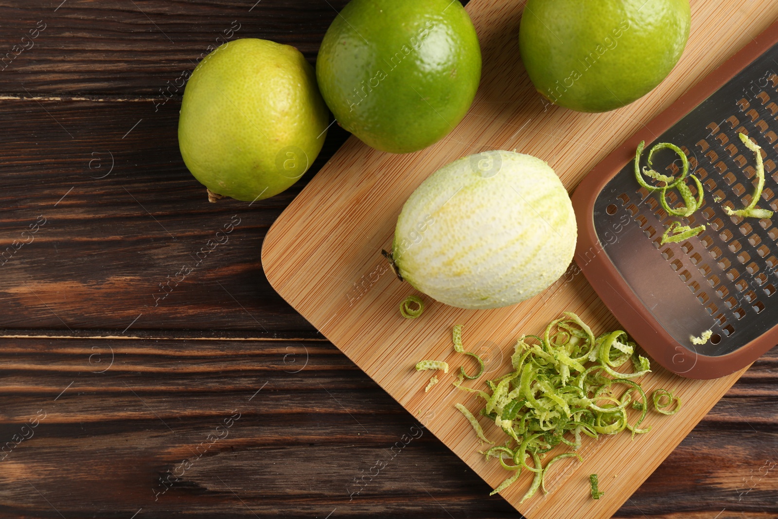 Photo of Lime zest, grater and fresh fruits on wooden table, flat lay. Space for text