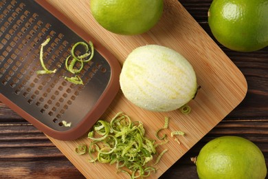 Photo of Lime zest, grater and fresh fruits on wooden table, flat lay