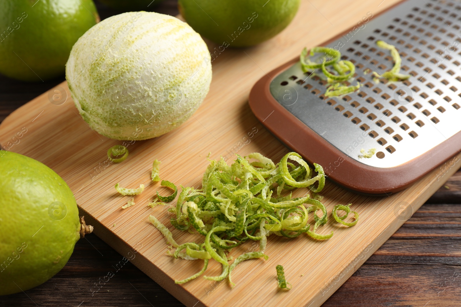 Photo of Lime zest, grater and fresh fruits on wooden table, closeup