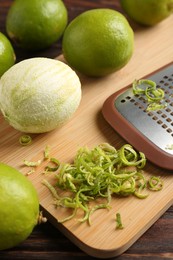 Photo of Lime zest, grater and fresh fruits on wooden table, closeup