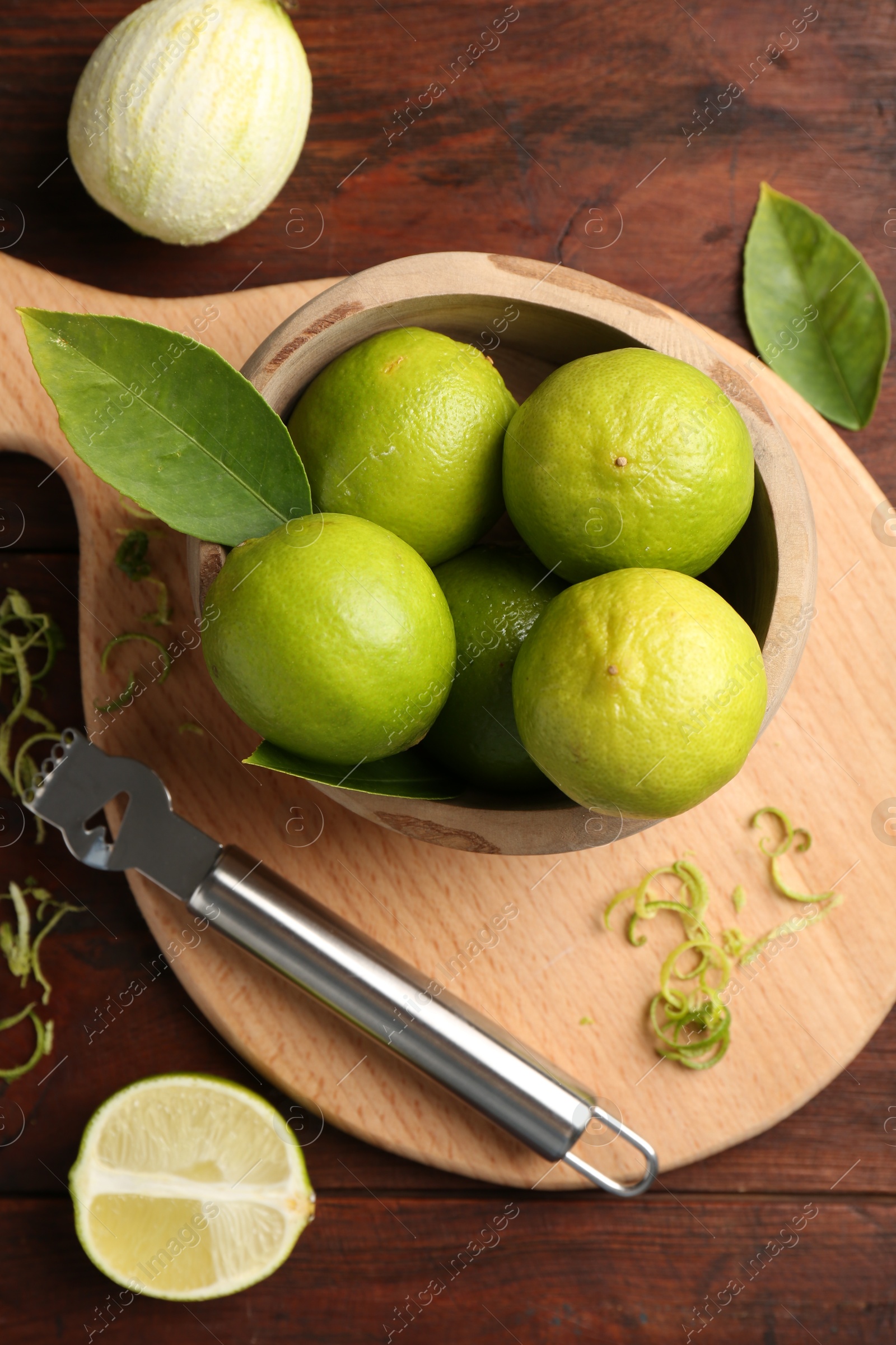 Photo of Lime zest, zester, leaves and fresh fruits on wooden table, flat lay